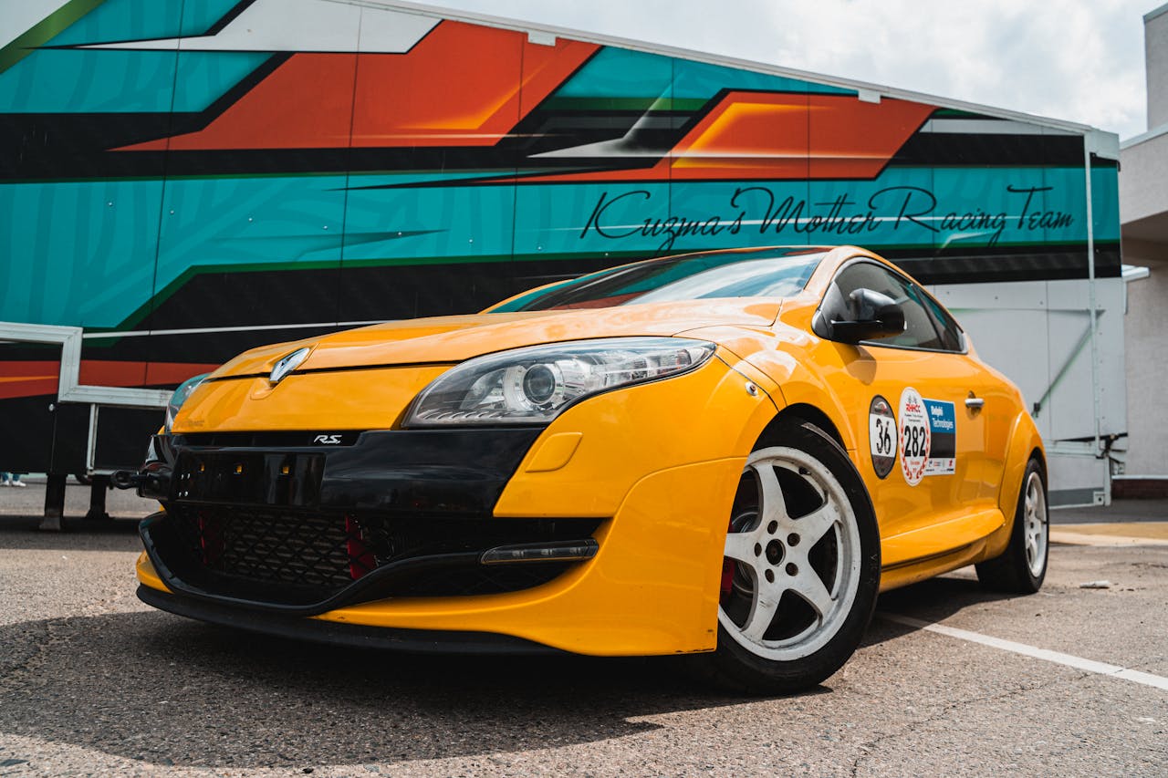 Close-up of a yellow Renault Megane RS car with racing decals, parked outdoors.