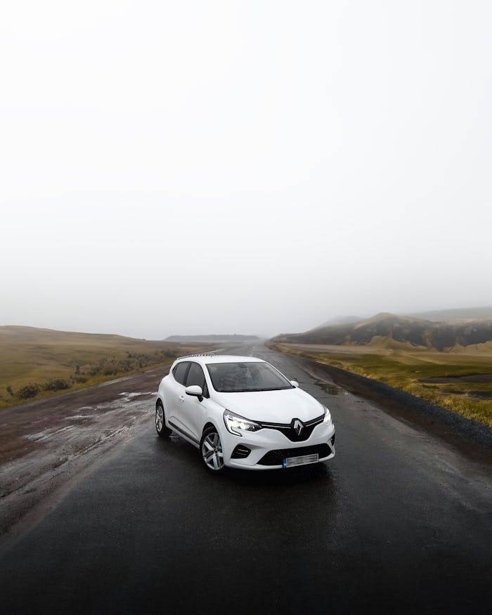 A sleek white Renault parked on a foggy road surrounded by mist-covered hills.